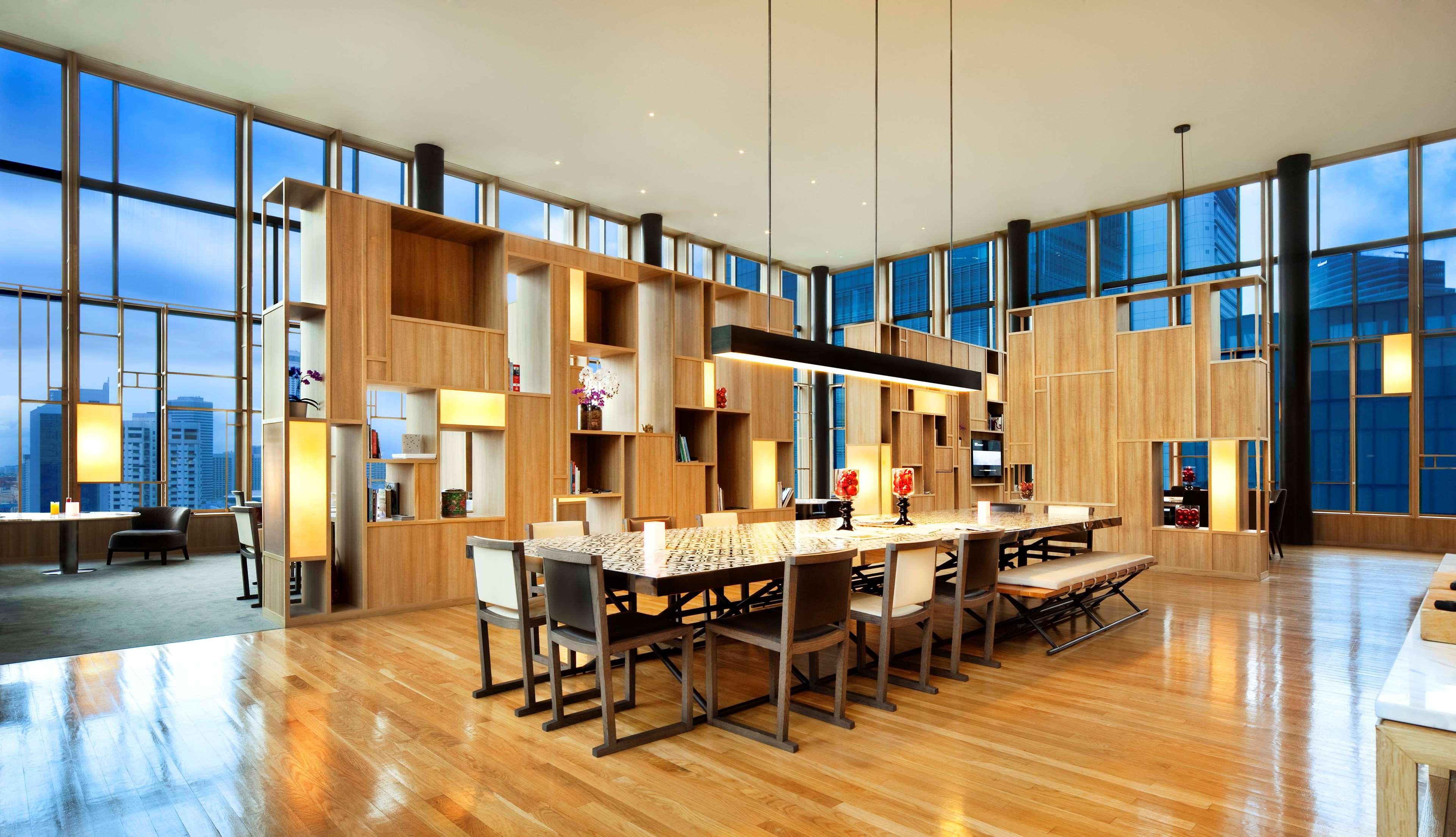 Parkroyal Collection Pickering, Szingapúr Kültér fotó The image shows a modern dining area or common space with an open layout. The room features large windows that allow natural light to flood in, enhancing the warm wooden tones of the décor. 

In the center, there is a long rectangular dining table su