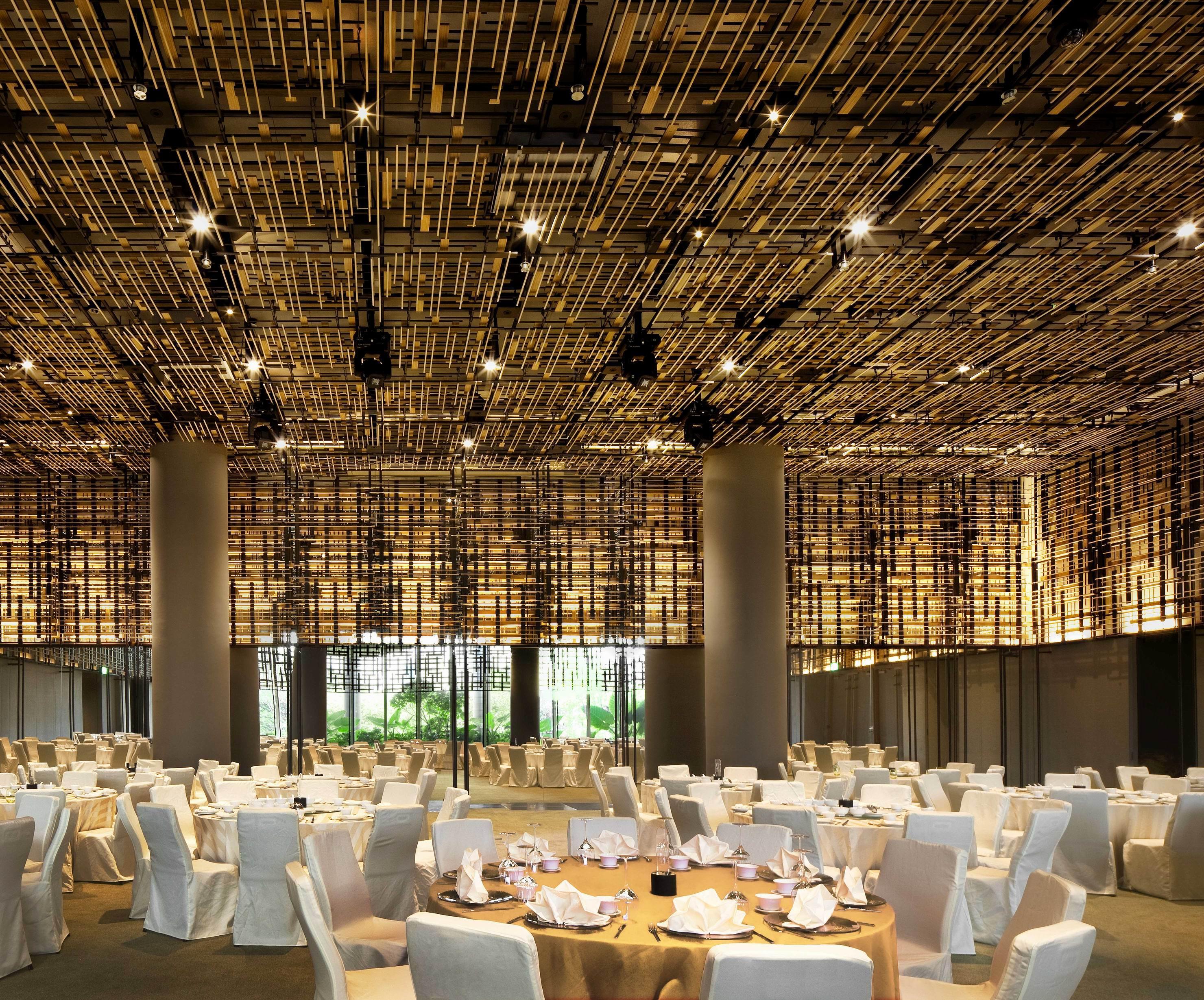 Parkroyal Collection Pickering, Szingapúr Kültér fotó The photo shows a spacious dining area with a modern and elegant design. The ceiling features a unique installation of bamboo or wooden elements that creates a textured appearance. The room is filled with round tables, each set with white tablecloths