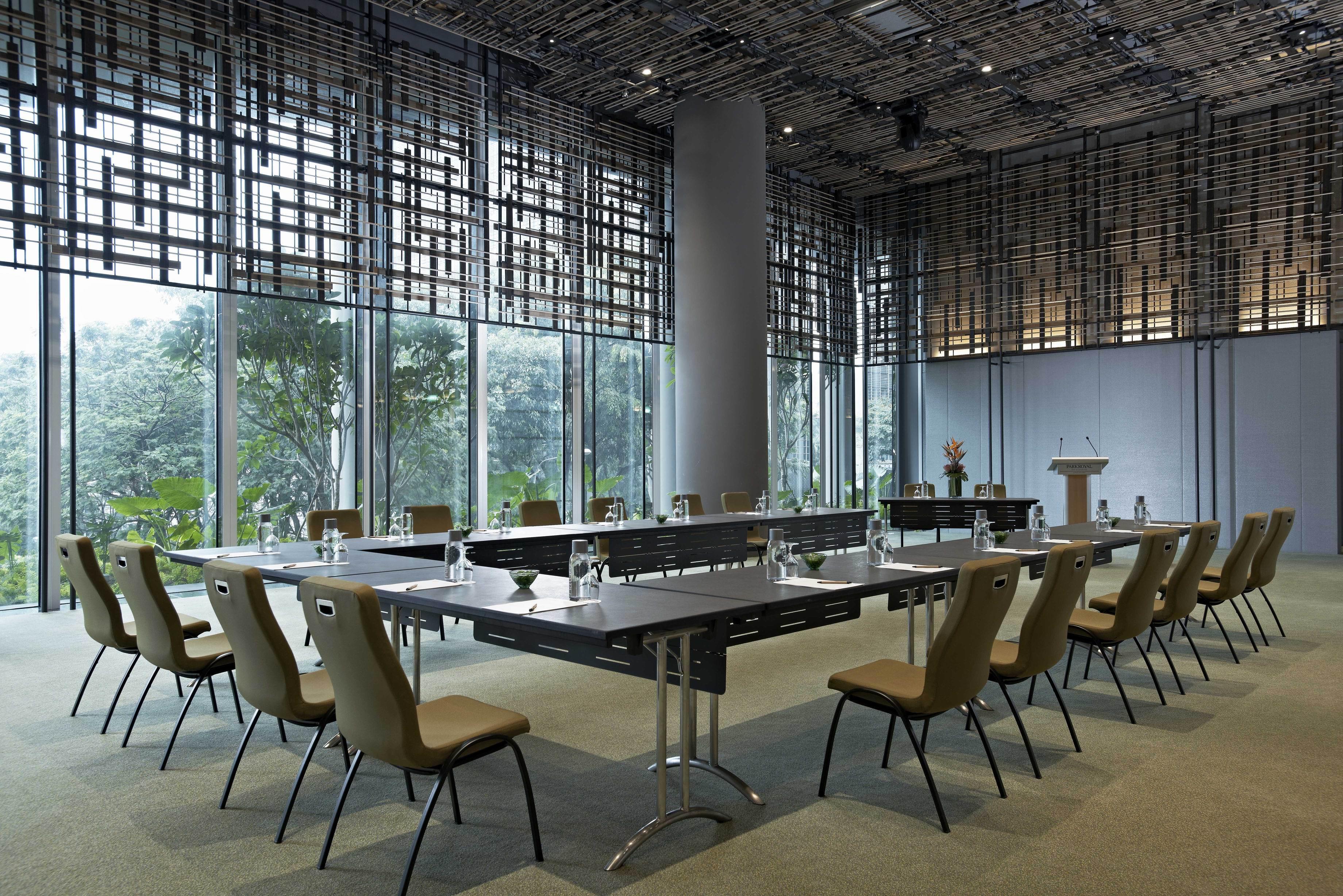 Parkroyal Collection Pickering, Szingapúr Kültér fotó The image shows a modern conference room. It features a long, rectangular table surrounded by several chairs. The table is equipped with glass water bottles and glasses. Large windows provide natural light and offer a view of greenery outside. The ro