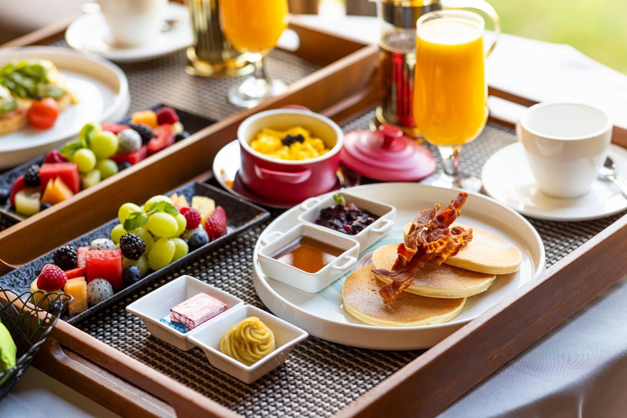 Parkroyal Collection Pickering, Szingapúr Kültér fotó The photo shows a beautifully arranged breakfast tray. It includes:

- A stack of pancakes served with crispy bacon.
- Small bowls of syrup and fruit preserves.
- Slices of fresh fruit, including a variety of berries and grapes.
- A small dish with w