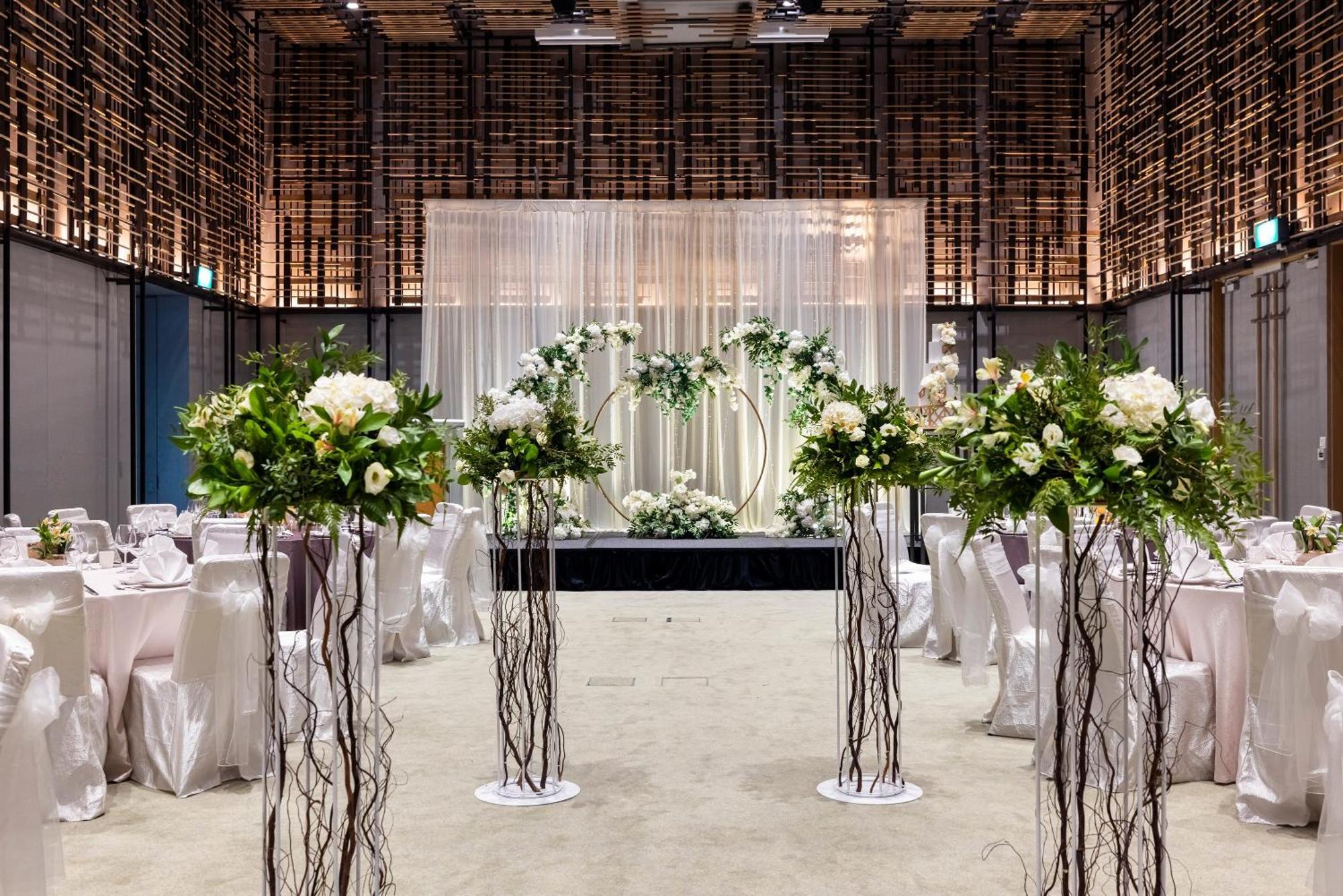 Parkroyal Collection Pickering, Szingapúr Kültér fotó The photo shows a beautifully decorated event space, likely set up for a wedding. In the center, there is an elegant backdrop made of draped fabric, creating a soft and romantic atmosphere. Flanking the backdrop are floral arrangements positioned on 