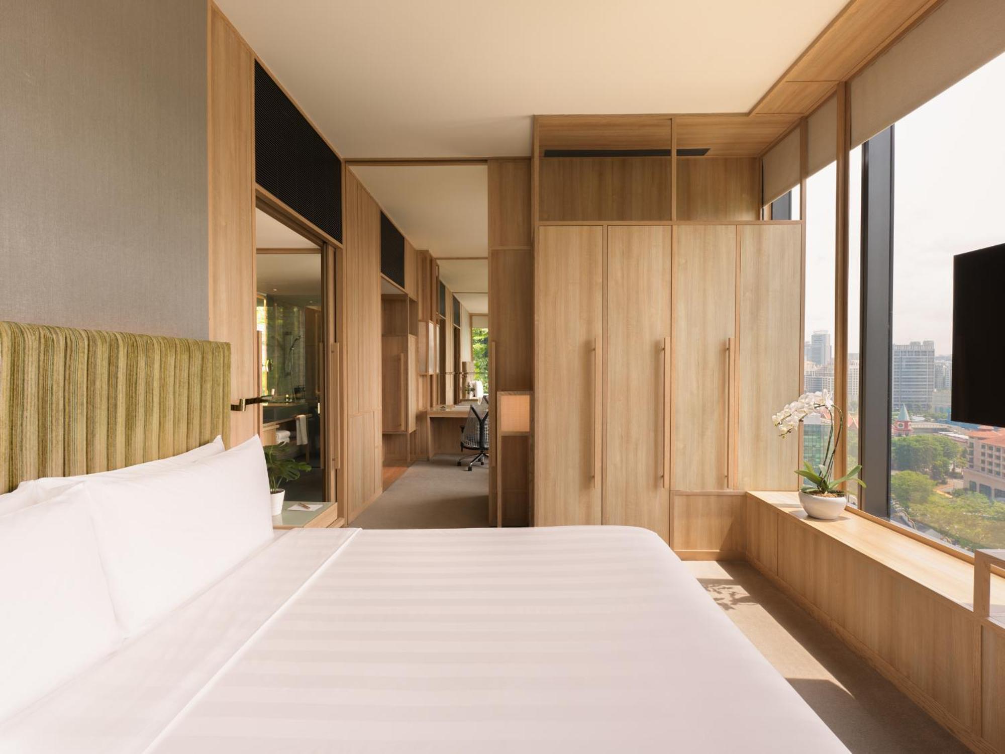 Parkroyal Collection Pickering, Szingapúr Kültér fotó The photo shows a modern hotel room featuring a simple design with a focus on natural materials. There is a large bed with white bedding positioned against a wall, which has a textured green headboard. On one side of the room, there are wooden cabine