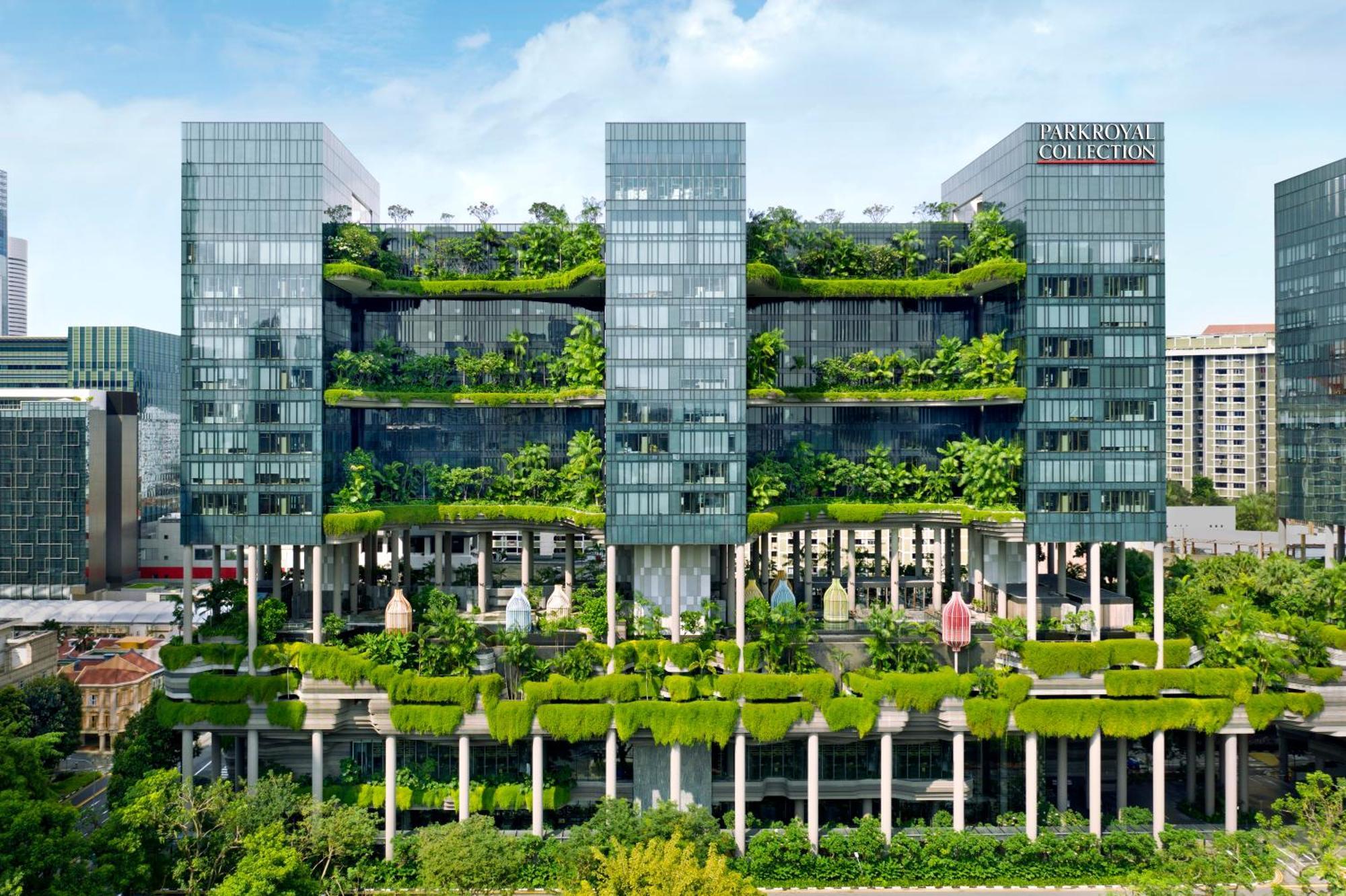 Parkroyal Collection Pickering, Szingapúr Kültér fotó The photo shows a modern multi-story building characterized by a sleek, glass facade. The structure features multiple floors with abundant greenery, including vertical gardens and terraces filled with plants, creating a striking contrast between the 